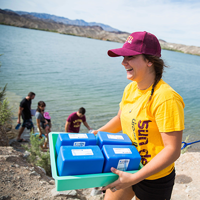 ASU Lake Havasu student at the edge of the Colorador River holding lab test kits.