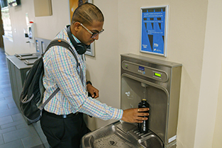 Man at a wall-mounted drinking fountain filling water bottle at the bottle refiller station.