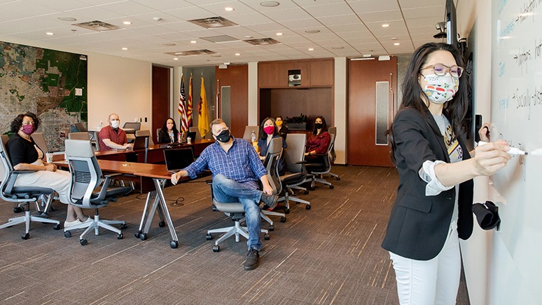Staff meeting held in a confrence room, physical distancing, wearing face coverings.